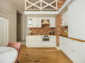 A compact kitchen with white cabinetry, a brick accent wall, and a wooden floor.