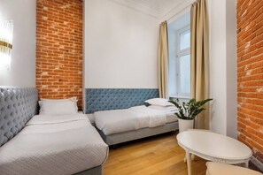 Une pièce avec un mur en briques, un canapé gris recouvert de tissu, un lit avec une tête de lit bleue, une petite table blanche et une plante en pot.