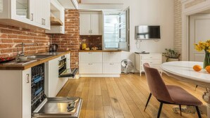 A compact kitchen with a brick wall, white cabinetry, a dining table with chairs, and a flat-screen TV. - Magnifique 2-bed apartment (Kraków – Old Town)