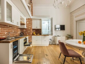 Une cuisine compacte avec un mur en briques, des meubles blancs, une table à manger avec des chaises et un téléviseur à écran plat.