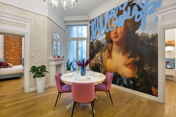 A dining area with a round table, chairs, and a large painting on the wall.