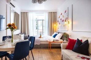 A hotel room with a dining area, a sofa, a coffee table, and a large window with curtains. - Poppy studio with balcony (Kraków)