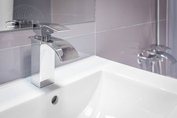 Un baño moderno con grifo cromado, lavamanos blanco y zona de ducha.