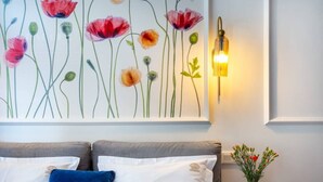 A bedroom with a bed, pillows, a wall-mounted light, and a floral painting. - Poppy studio with balcony (Kraków)