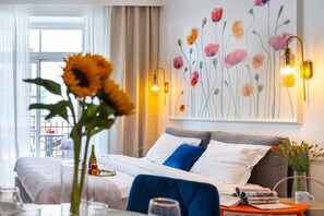 Habitación de hotel con cama, una mesa con un jarrón de flores, una lámpara de pared y un cuadro floral.