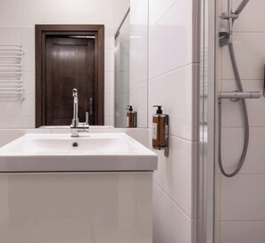 Un baño con un lavamanos blanco, ducha y puerta de madera.