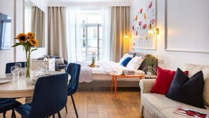 A hotel room with a dining area, a sofa, a coffee table, and a large window with curtains. - Poppy studio with balcony (Kraków)