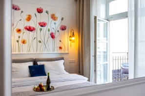 A hotel room with a bed, a painting of flowers, a nightlight, and a balcony with a chair. - Poppy studio with balcony (Kraków)
