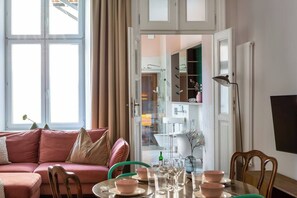 Una sala de estar moderna con un sofá rosa, una mesa de comedor preparada para cuatro personas y vista a la cocina.