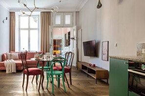A modern living room with a sofa, dining table, chairs, a TV, and a kitchen area with a Bosch oven. - Apartment Pink Velvet with sauna and bathtub (Kraków)