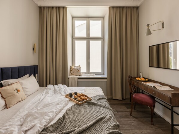 Habitación de hotel con cama, escritorio, silla, ventana con cortinas y una bandeja de pasteles.