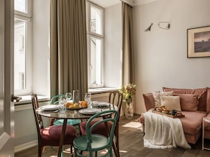 A dining area with a table set for four, chairs, a vase with flowers, and a sofa with cushions.