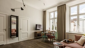A living room with a sofa, a dining table with chairs, a TV, and a window with curtains. - Blue Suede apartment (Kraków – Old Town)