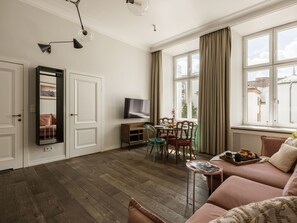 A living room with a sofa, a dining table with chairs, a TV, and a window with curtains. - Blue Suede apartment (Kraków – Old Town)