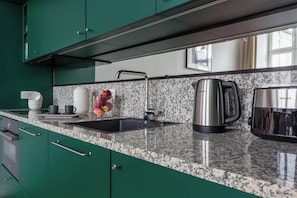 A kitchen with green cabinets, a granite countertop, a sink, a kettle, and a toaster.