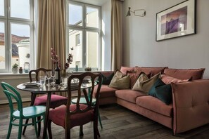 A living room with a sofa, chairs, a dining table set, and a window with curtains. - Blue Suede apartment (Kraków – Old Town)