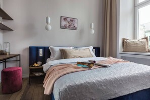A bedroom with a bed, bedside tables, a window with curtains, and a wall-mounted picture.