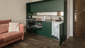 A compact kitchen with green cabinets, a built-in oven, and a dishwasher. - Blue Suede apartment (Kraków – Old Town)