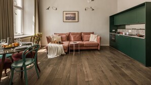 A dining area with a table set for two, a sofa, and a kitchen with green cabinets. - Blue Suede apartment (Kraków – Old Town)