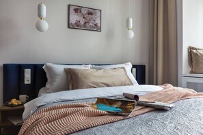 A neatly made bed with a blue headboard, a beige pillow, and a pink knitted blanket. - Blue Suede apartment (Kraków – Old Town)