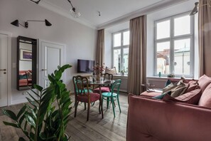 A living room with a sofa, dining table, chairs, a TV, and large windows. - Blue Suede apartment (Kraków – Old Town)