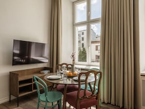 A dining area with a table set for four, a television mounted on the wall, and a window with curtains.