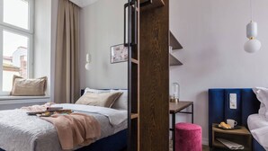 A modern hotel room with a bed, bedside table, nightstand, and a window with curtains. - Blue Suede apartment (Kraków – Old Town)