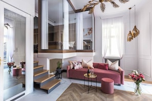 A modern living room with a pink sofa, a coffee table, and a staircase leading to an upper level.