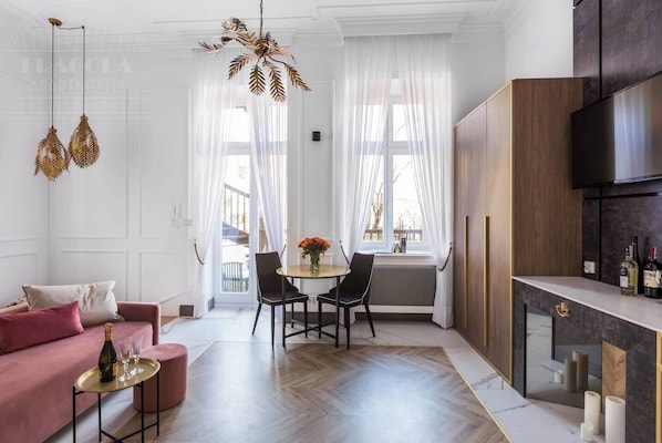 A modern living room with a sofa, a dining table with chairs, a kitchen area with a TV, and a decorative chandelier.