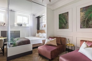A modern hotel room with a bed, a sofa, a small table with glasses, and artwork on the walls.