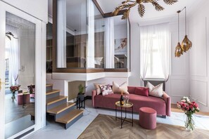 Een moderne woonkamer met een roze bank, een salontafel en een trap naar een hoger gelegen verdieping.