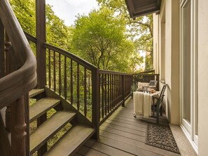 A wooden deck with a railing, a bench, and a door leading to a building.
