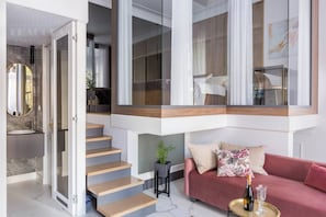 A modern apartment with a staircase, a pink sofa, a small table with a bottle, and a mirror.