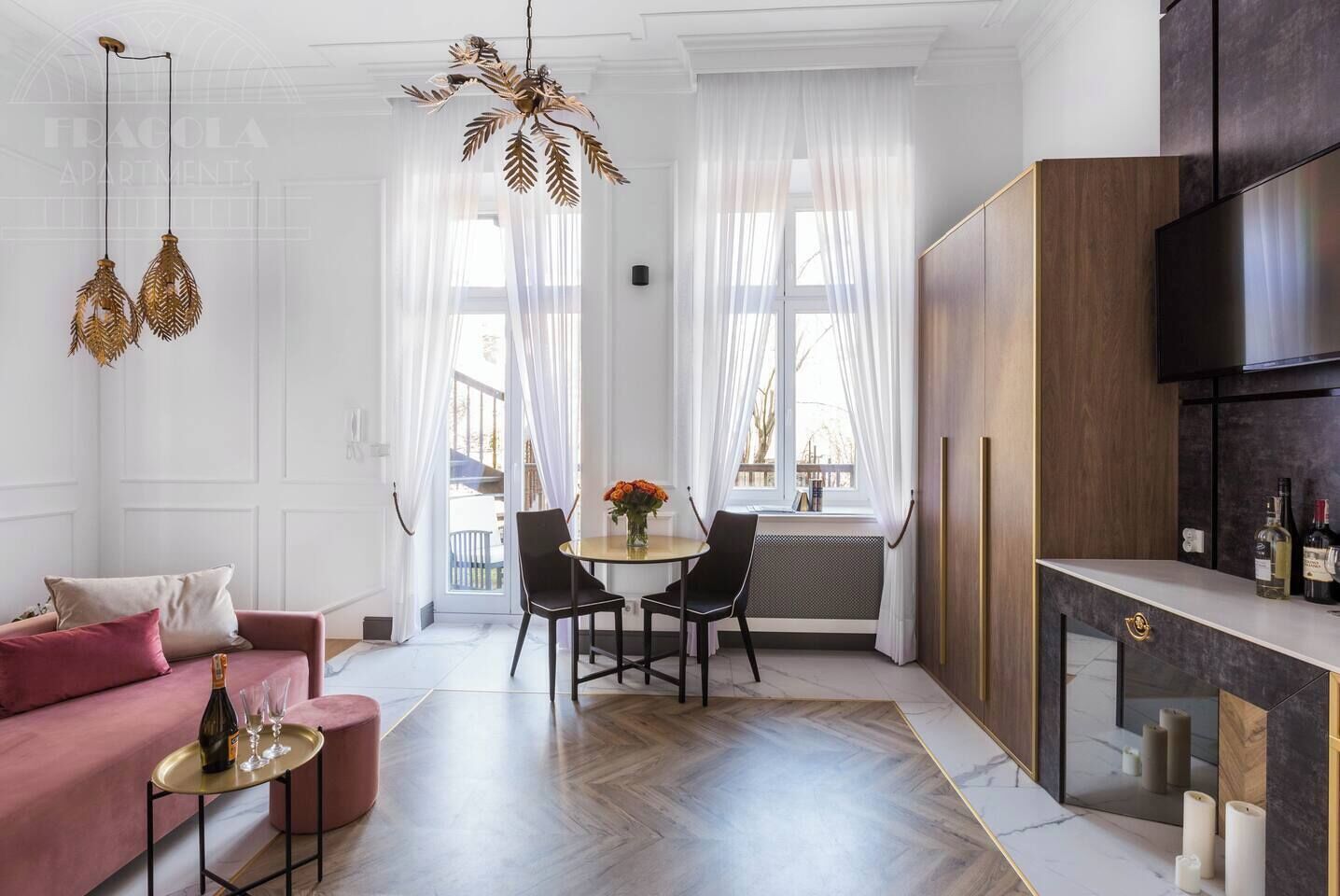 A modern living room with a sofa, a dining table with chairs, a kitchen area with a TV, and a decorative chandelier.