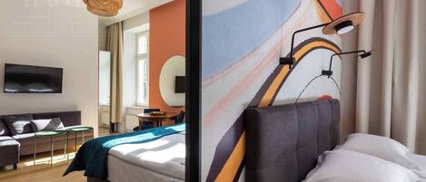 A modern hotel room with a bed, a TV, a dining area, and a large abstract wall mural.