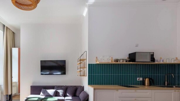 A modern living room with a sofa, a television, and a kitchen area with a microwave and sink. - Funky studio 10 min to Main Square (Kraków – Old Town)