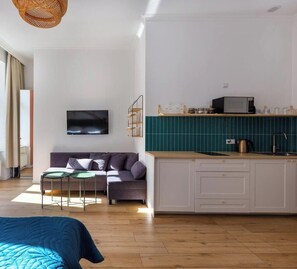 Un salon moderne comprenant un canapé, un téléviseur et un coin cuisine avec un four à micro-ondes et un évier.