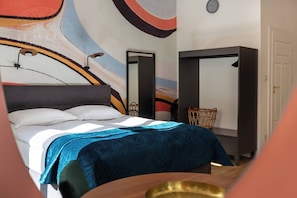 A bedroom with a bed, a chair, a wardrobe, and a wall with abstract art.
