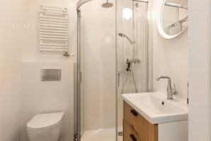 Een moderne badkamer met een douchecabine van glas, een wit toilet en een wastafel met spiegel.