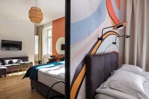 A modern hotel room with a bed, a TV, a dining area, and a large abstract wall mural. - Funky studio. - One Bedroom Apartment, Sleeps 2 (Kraków – Old Town)