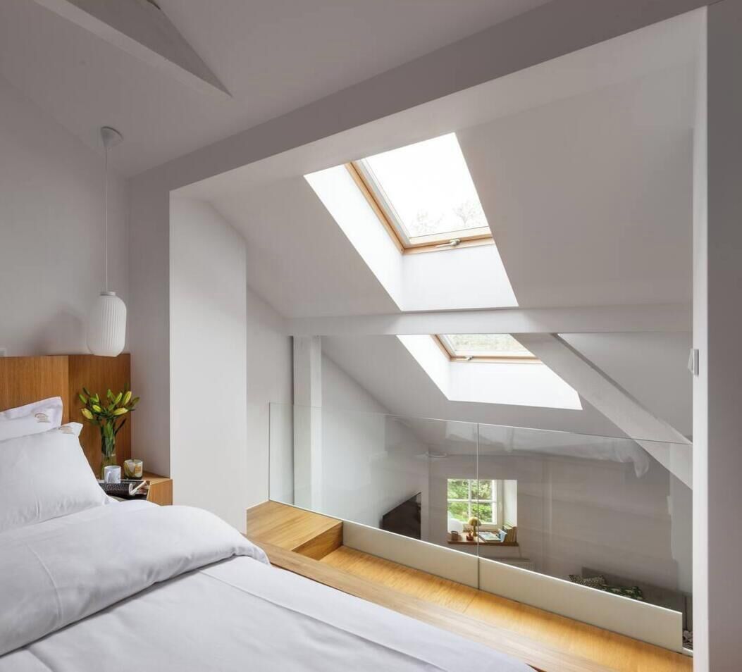 A modern bedroom with a skylight, a bed, a bedside table, and a view of a balcony.