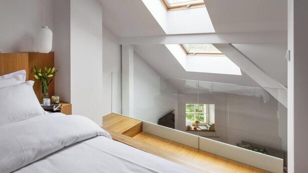 Une chambre à coucher moderne avec un puits de lumière, un lit, une table de chevet ornée d’un vase de fleurs et une vue sur l’extérieur grâce à un mur de verre.