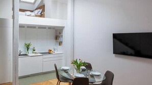 Une cuisine moderne avec des meubles blancs, une table à manger avec des chaises et un téléviseur à écran plat fixé au mur.