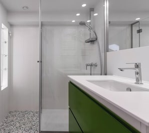 Un baño moderno con cabina de ducha de vidrio, un lavabo blanco y un mueble verde.