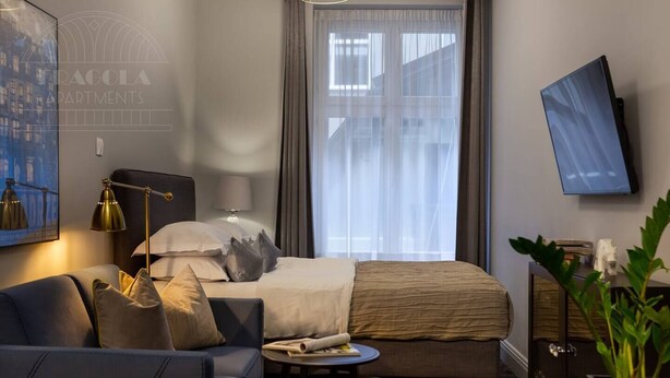 A hotel room with a bed, a sofa, a desk, a lamp, a TV, and a window with curtains.