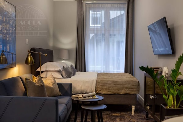 A hotel room with a bed, a sofa, a desk, a lamp, a TV, and a window with curtains.