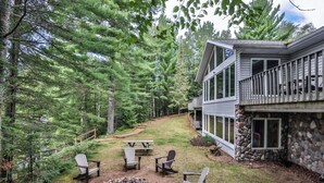 A cabin with a stone exterior, a deck, and a fire pit surrounded by Adirondack chairs. - Stepaway Vacation Rentals- Whitewoods Cove (St Germain)