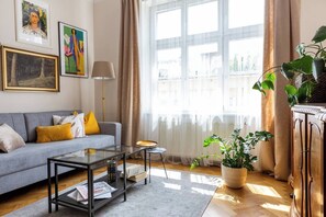 A modern living room with a grey sofa, a glass coffee table, and a large window with curtains. - Antique 1-bed apartment (Kraków – Old Town)