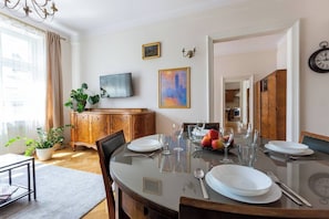 Un comedor con una mesa redonda dispuesta para cuatro personas, un televisor montado en la pared y un reloj en la pared.