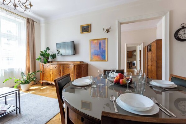 Un comedor con una mesa redonda dispuesta para cuatro personas, un televisor montado en la pared y un reloj en la pared.